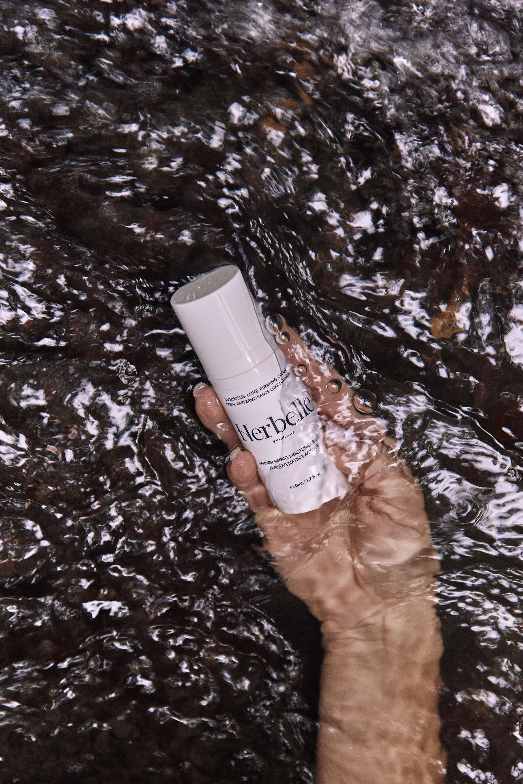 White bottle of Herbelle Skincare being held under flowing water