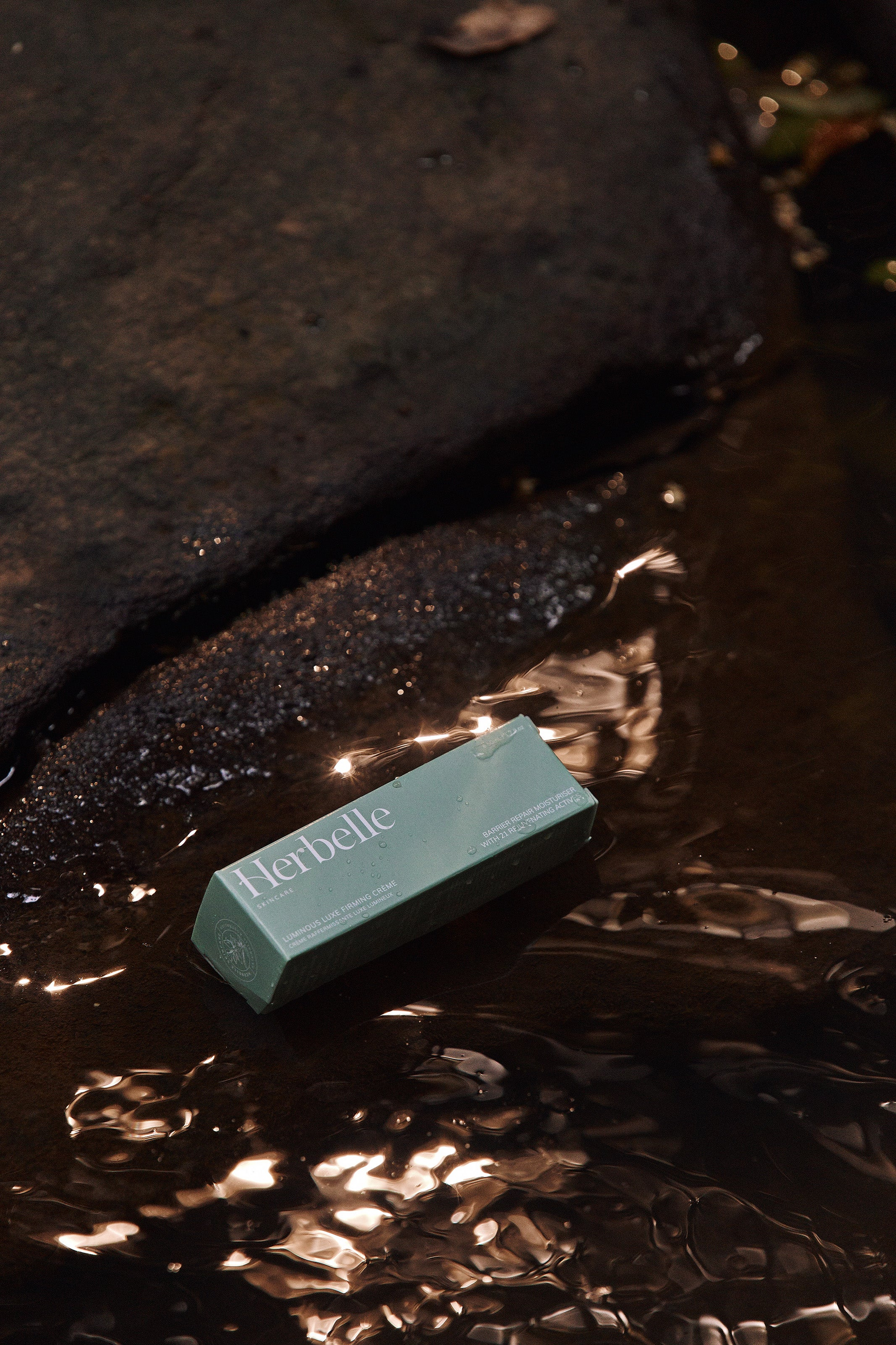 Boxed up herbelle skincare product sitting on shinning rock with water flowing