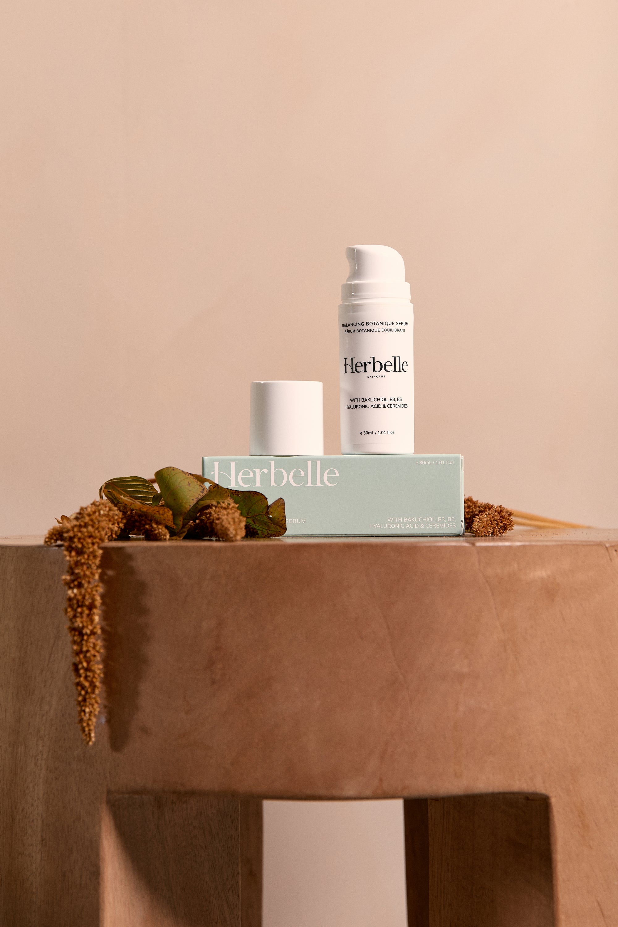 Herbelle skincare bottle sitting on an earth coloured stool with floral wear placed around it