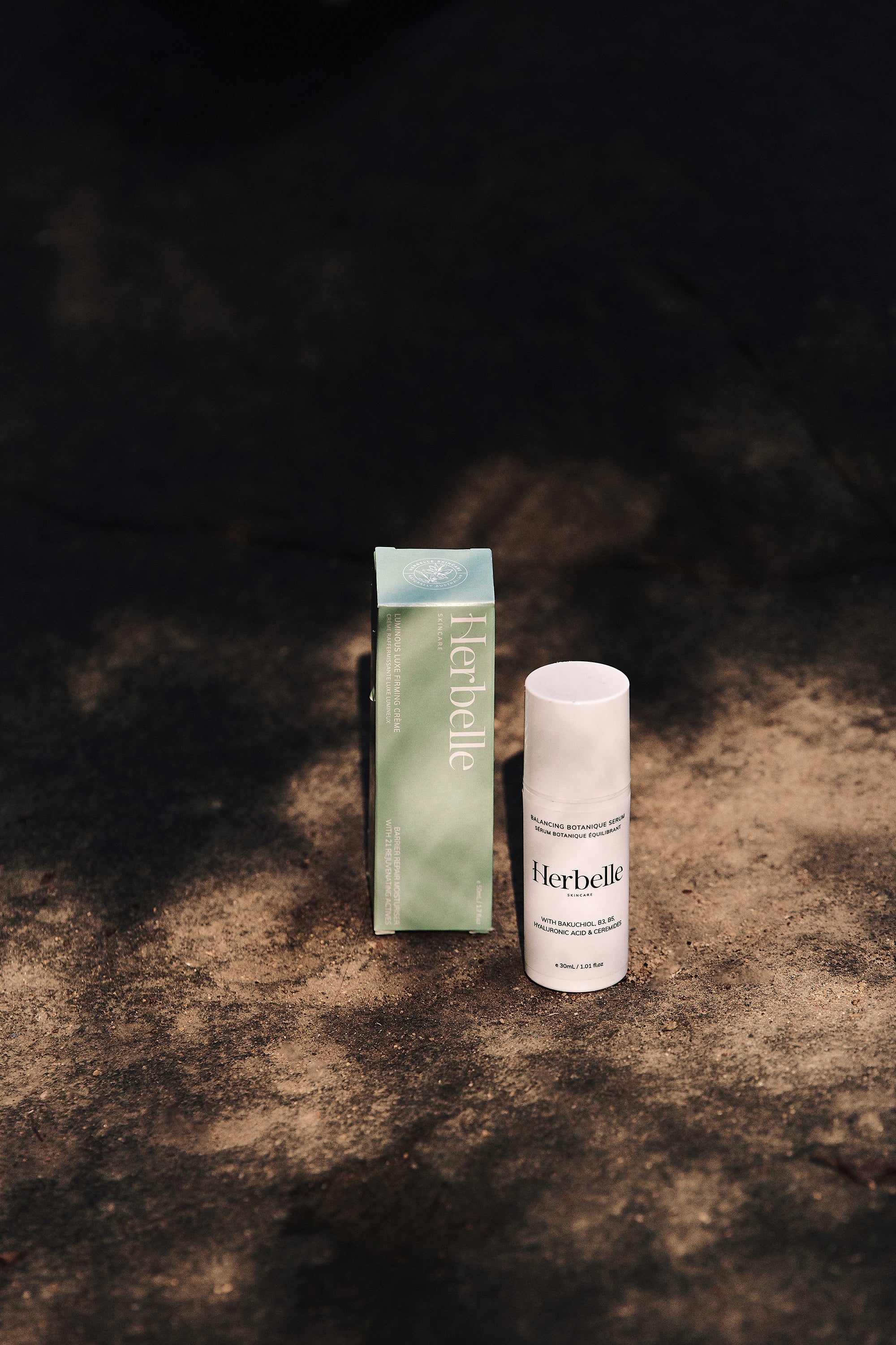 Herbelle skincare bottle sitting nect to box on a rock half covered by shade.